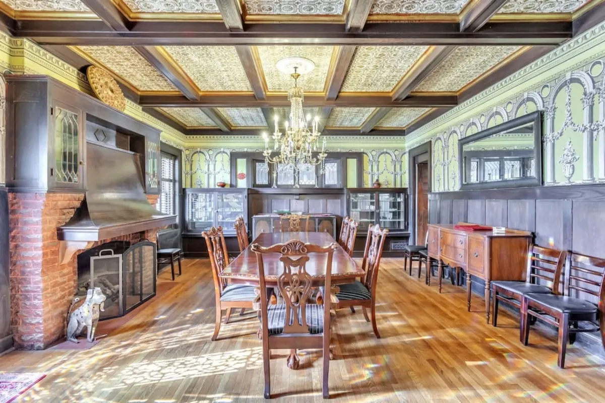 A sophisticated dining room with a gleaming chandelier, formal dining table, fireplace, and decorative wall panels. The room captures the grandeur of shared meals, celebrations, and elegant events.