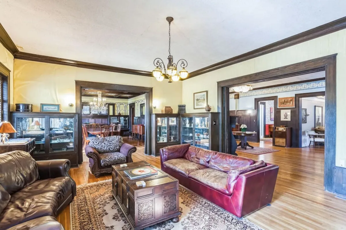 This image highlights a plush lounge area adorned with leather sofas, a decorative coffee table, a chandelier, and elegant display cabinets. The natural light floods the space, making it feel open and conducive to both conversation and relaxation.