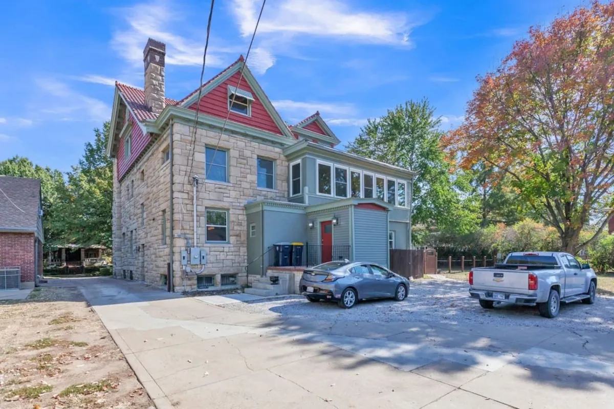 This image shows a grand historic stone facade with a colorful roof, large windows, and mature trees framing the exterior. The inviting porch suggests opportunities for relaxing outdoors, with plenty of space for gatherings or simply enjoying the morning sun.