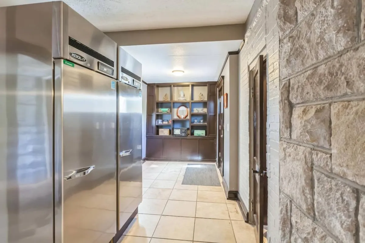 This kitchen scene highlights dual stainless steel refrigerators and an open shelving unit against a textured wall. The space is clearly designed for efficient cooking and large-scale meal preparation, reflecting the robust storage and cooking capabilities described in the section.