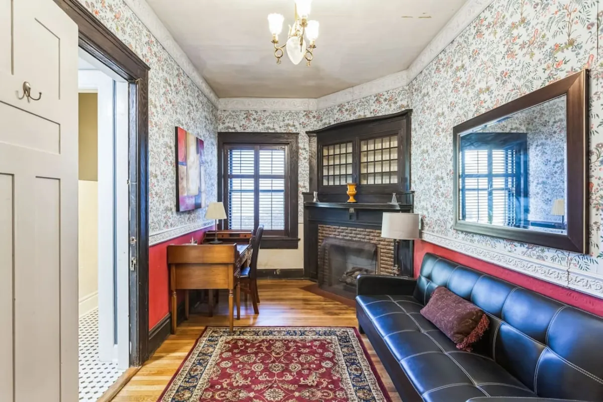 A nostalgic and warm room combining a fireplace, a comfortable sofa, a desk for writing, and floral wallpaper. It balances productivity with comfort, offering a spot for reading, writing, or relaxed conversation.