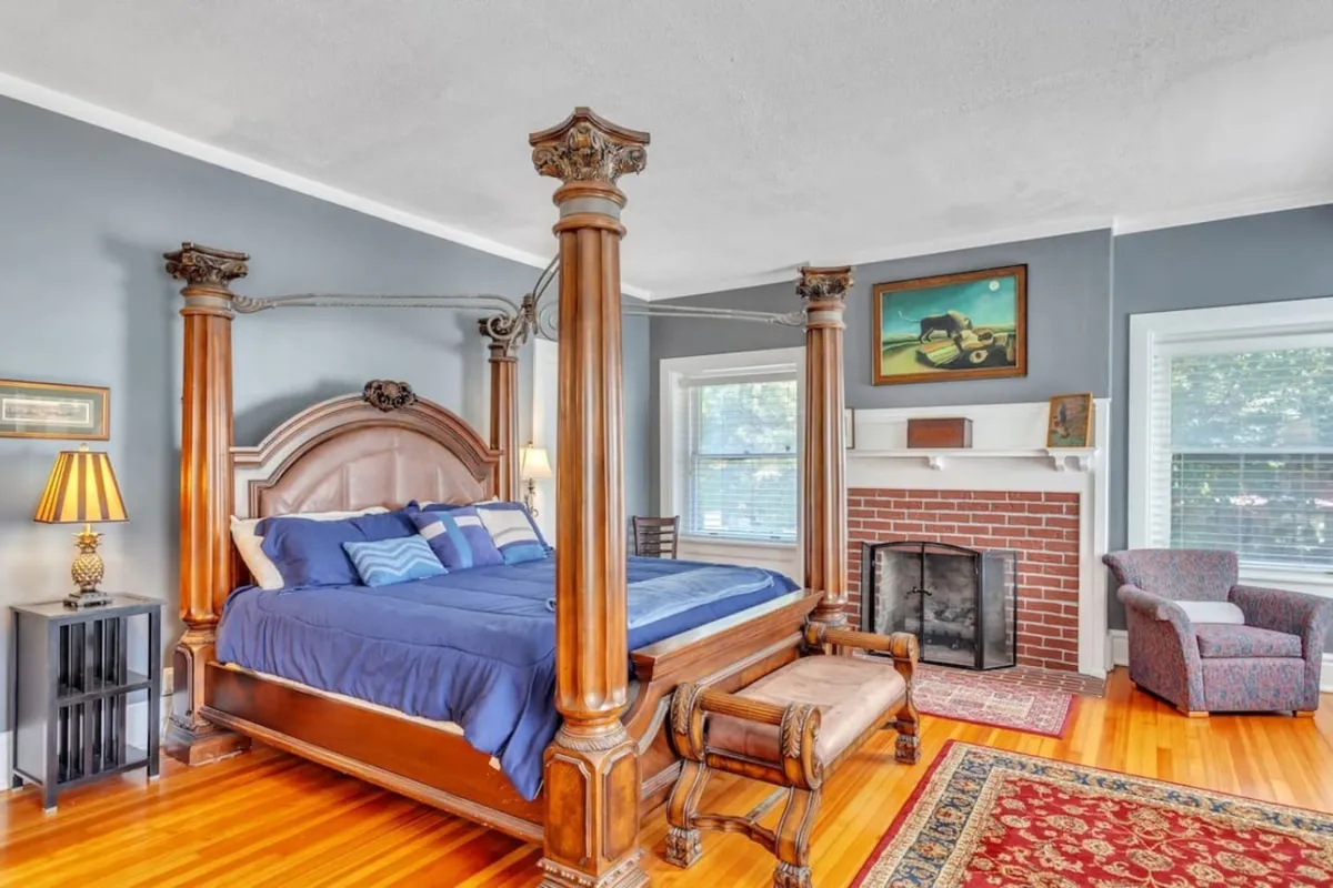This image shows a spacious bedroom featuring a four-poster king-size bed, a classic fireplace, an inviting armchair, and a decorative rug. The style exudes period detailing with elegant touches and a soothing, comforting ambiance—ideal for restful retreats after a day of adventures.
