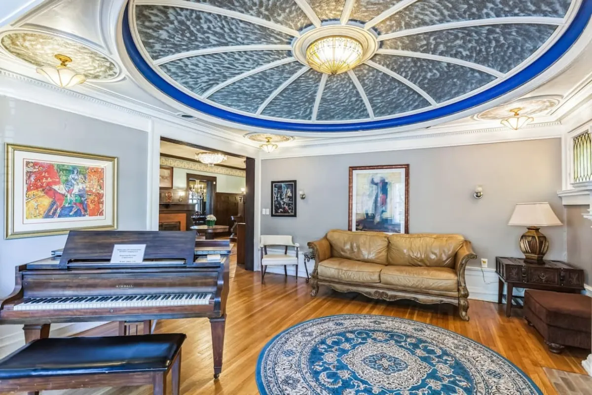A sophisticated interior living space showcasing a grand piano, plush sofa, decorative ceiling, and tasteful artwork. The room exudes a welcoming, upscale ambiance ideal for socializing or small gatherings before a night out.