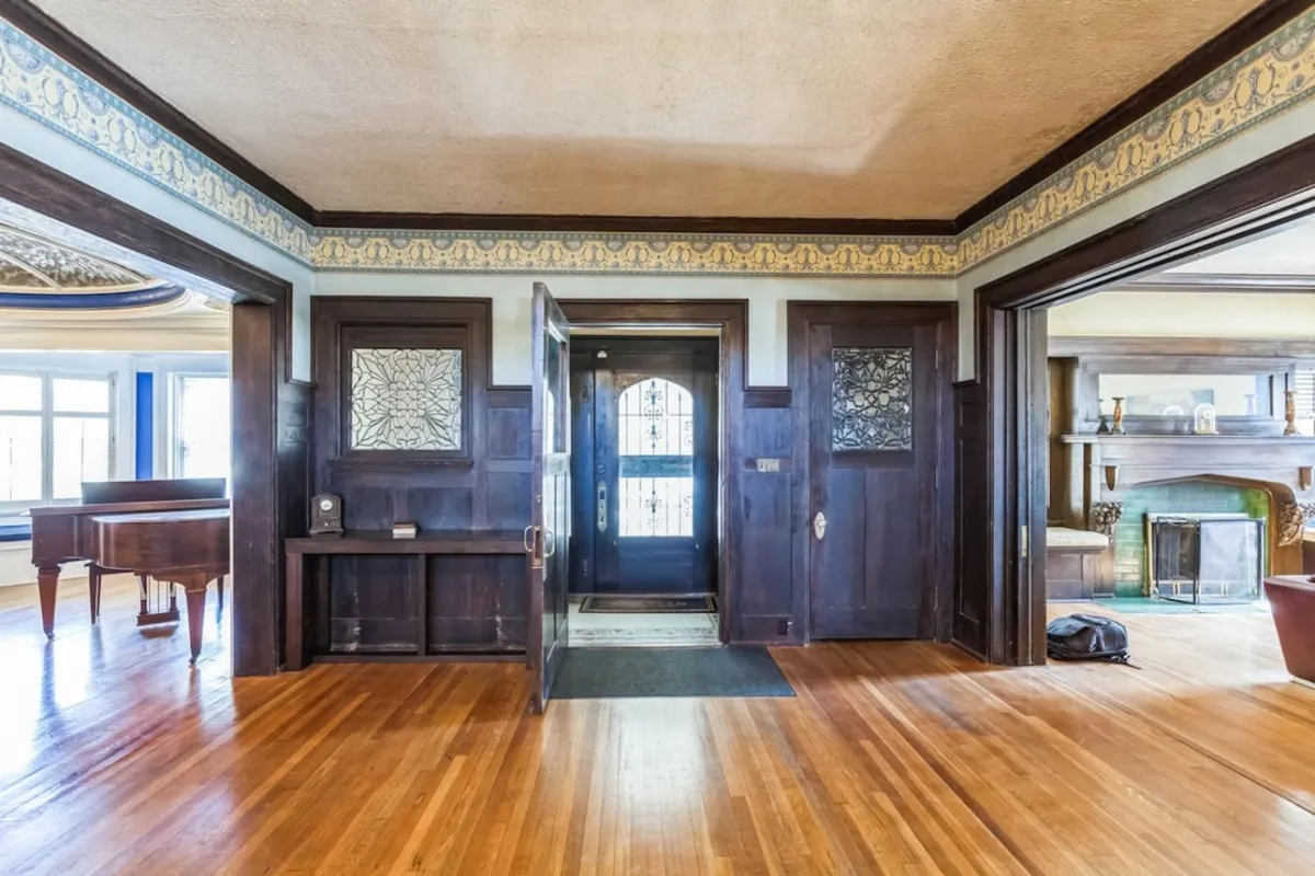 This image captures the entryway with rich wooden paneling, stained glass details, and a piano. The scene exudes warmth and elegance, immediately setting a tone of historic grandeur and inviting hospitality as guests are welcomed inside.