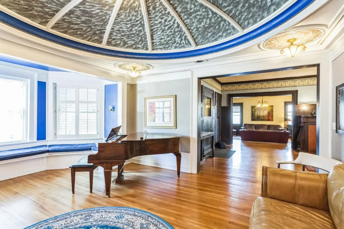 A sophisticated and warm gathering space featuring a grand piano, an ornate ceiling, a comfortable seating area, and prominent artwork. The room is set up for intimate concerts, lively social gatherings, or quiet reflection, making it a flexible multi-purpose area perfect for group activities or creative retreats.