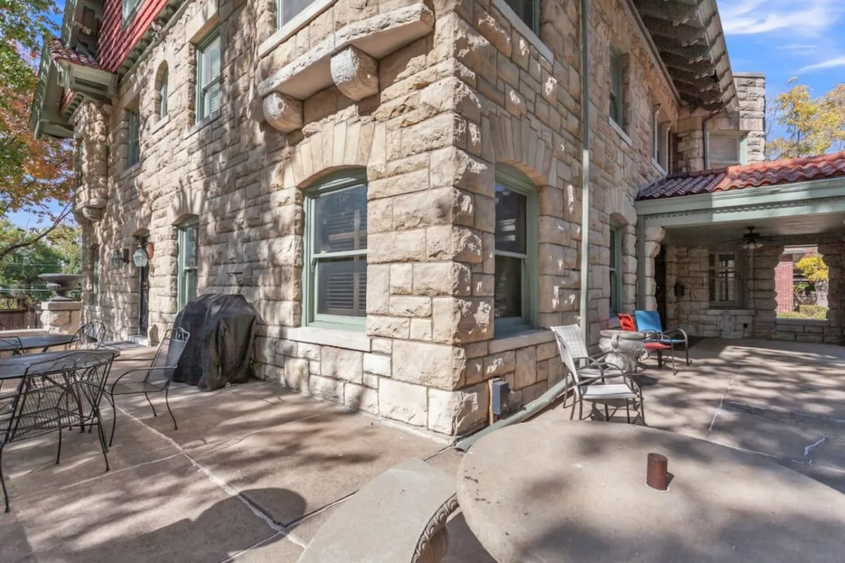 An exterior view highlighting a stone facade, large windows, and a cozy patio seating area. The patio is styled for comfort, suggesting possibilities for outdoor dining, relaxation, and socializing as the sun sets or rises.